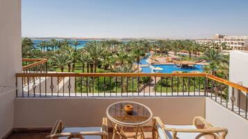 Un balcón con mesa y sillas, con vista a una piscina y palmeras.