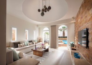 A spacious living room with a sofa set, a coffee table, and a TV mounted on a stone wall. - Fort Arabesque Resort, Spa & Villas (Makadi Bay)