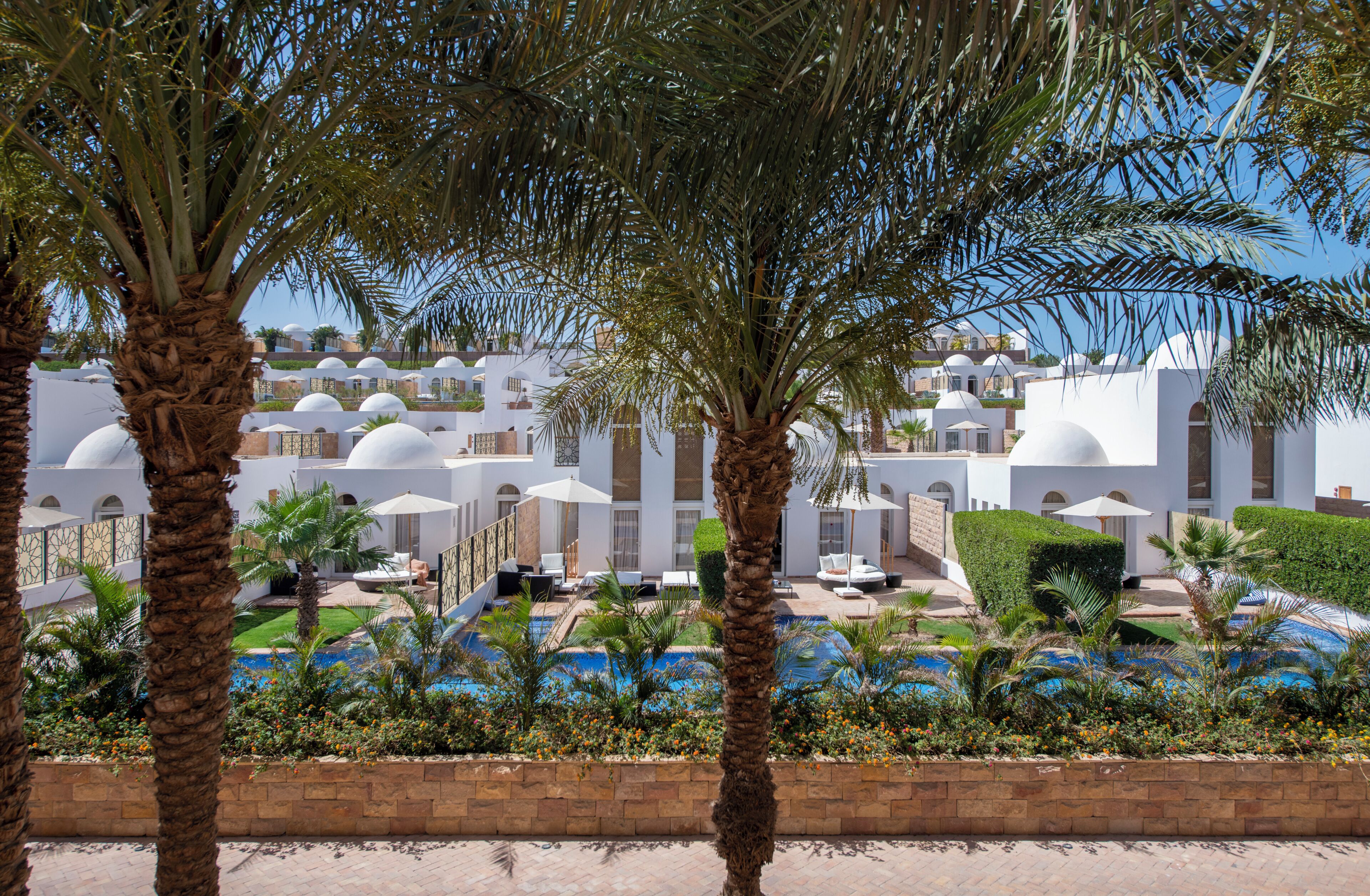 A resort with multiple white domed buildings, a swimming pool area, and palm trees.