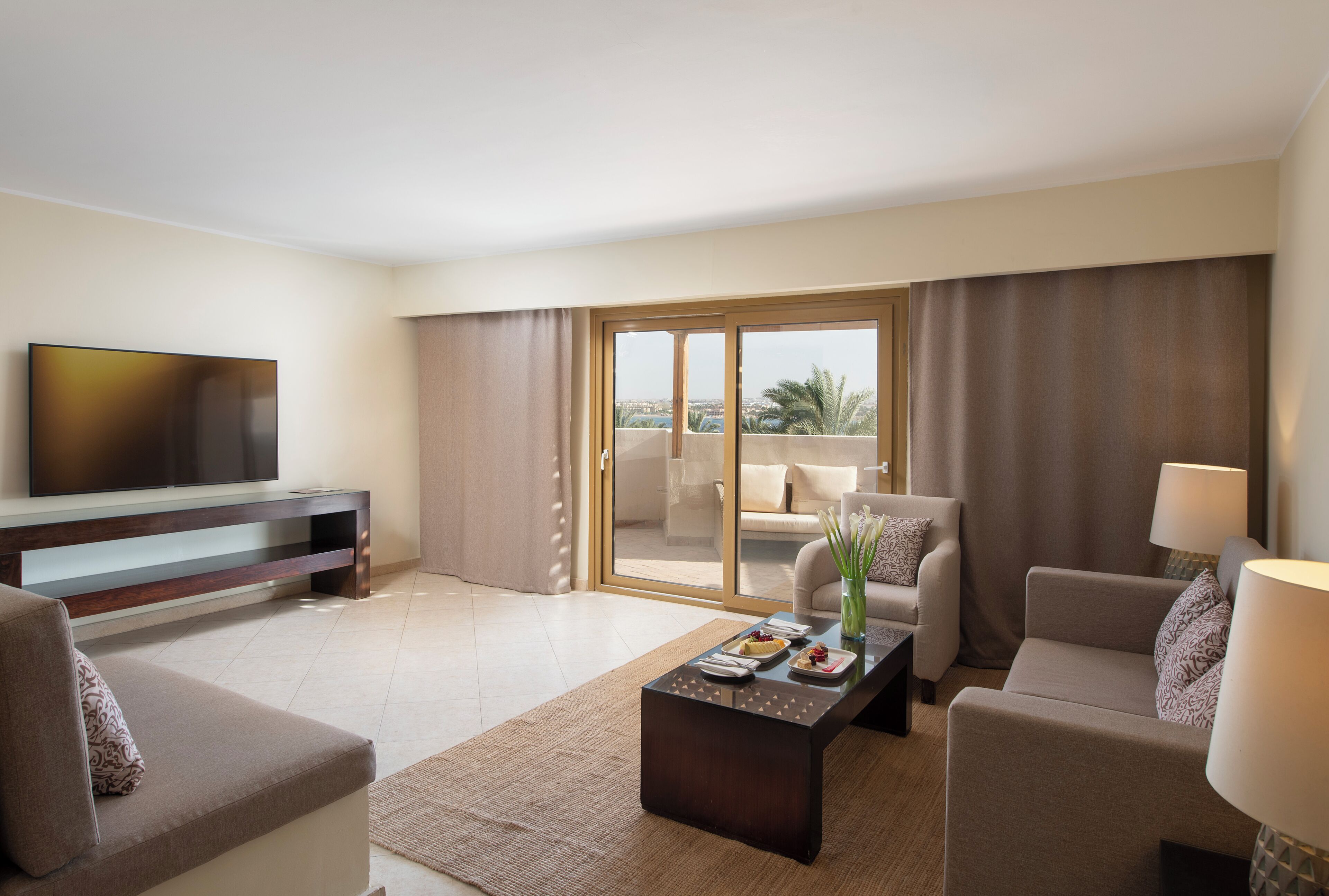 Ein Hotelzimmer mit Flachbildfernseher, einer Couch, einem Couchtisch, einem Sessel und einem Balkon mit Blick.
