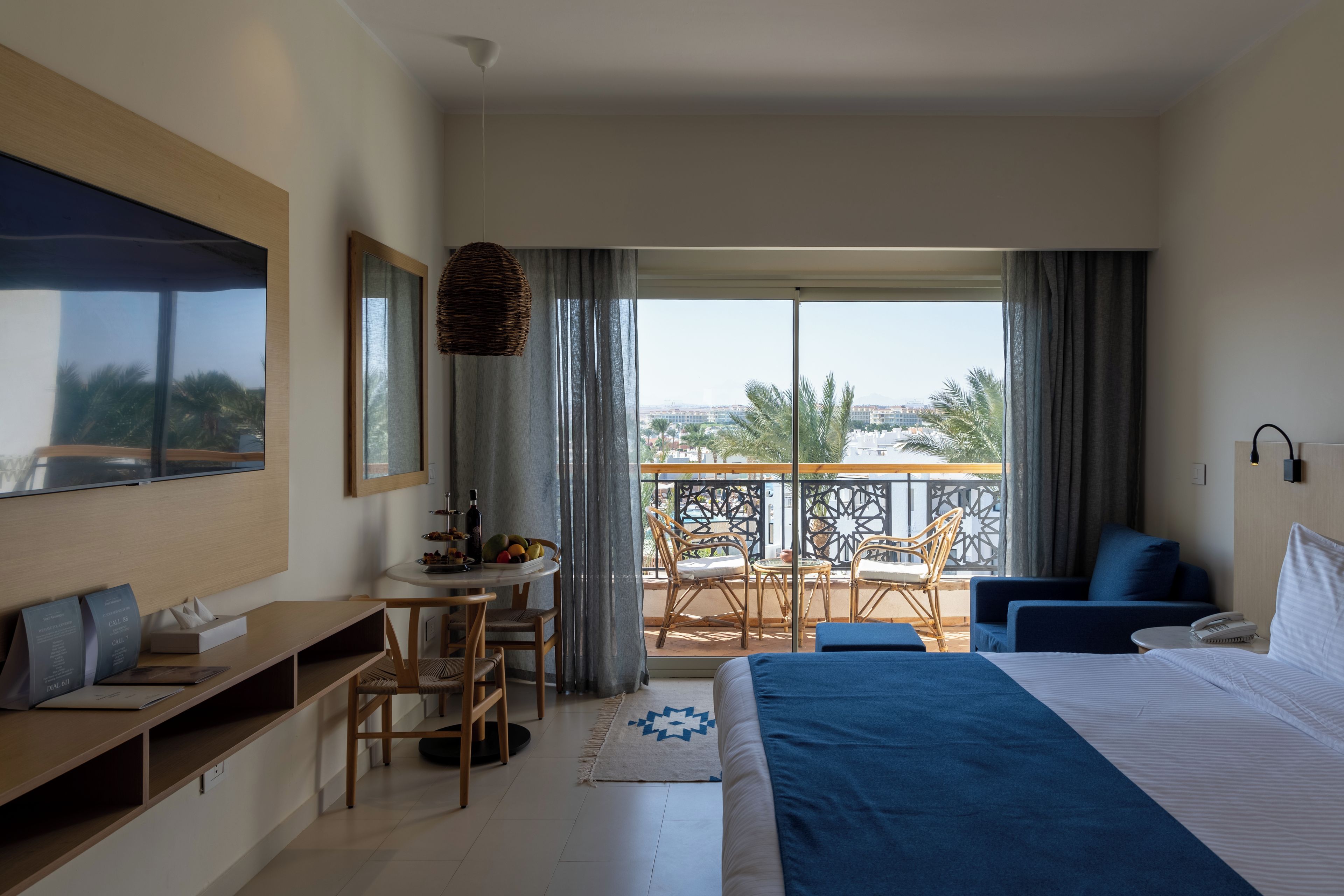 Habitación de hotel con cama, escritorio, silla, balcón con vistas y zona de comedor.