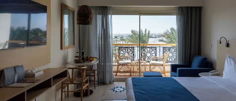 A hotel room with a bed, a desk, a chair, a balcony with a view, and a dining area.