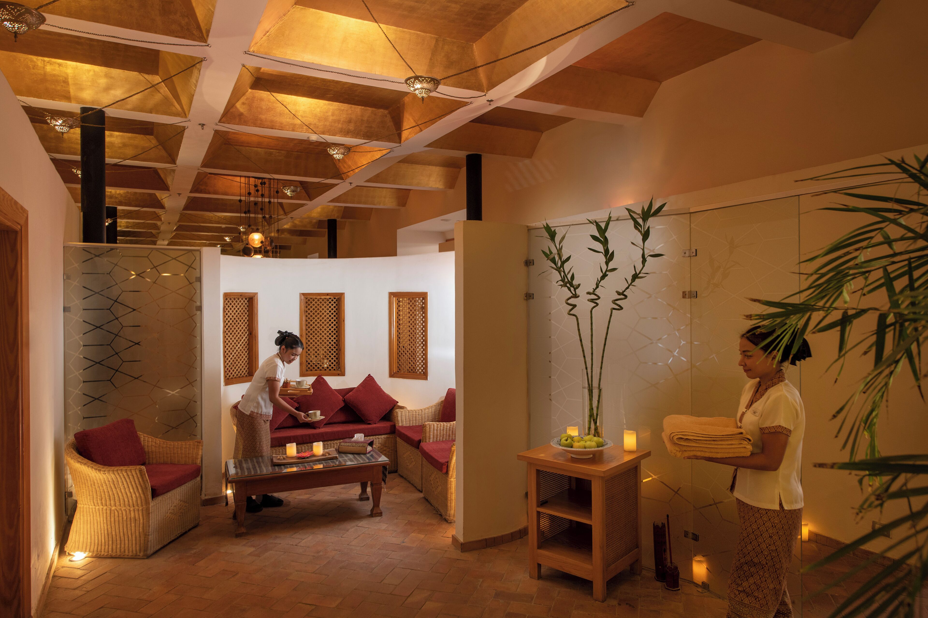 Een wellnessruimte met een houten plafond, een bank, een tafel met kaarsen en een wand met een geometrisch patroon.