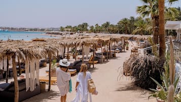 Un resort frente a la playa con sombrillas de paja, tumbonas y palmeras.