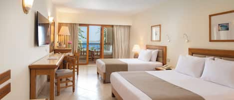 Quarto de hotel com duas camas, uma mesa, uma cadeira, televisão e varanda com vista.