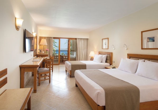 A hotel room with two beds, a desk, a chair, a TV, and a balcony with a view.