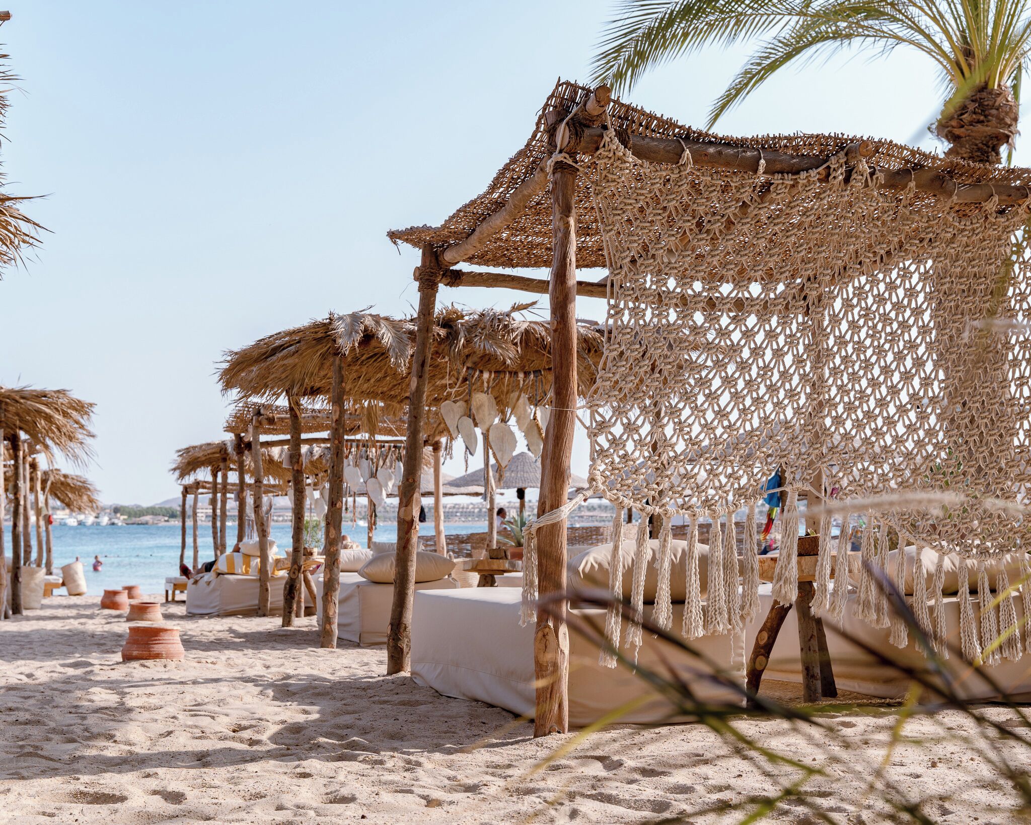 Ein Strand mit Reetsonnenstühlen und Holzbauten, feiner Sand und freie Sicht auf das Meer.