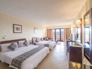 A hotel room with two beds, a desk, a TV, and a balcony with a view of buildings. - Fort Arabesque Resort, Spa & Villas (Makadi Bay)