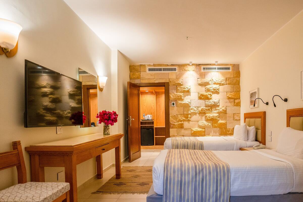 Ett hotellrum med två sängar, ett skrivbord, en stol, en spegel och en vägg av sten.