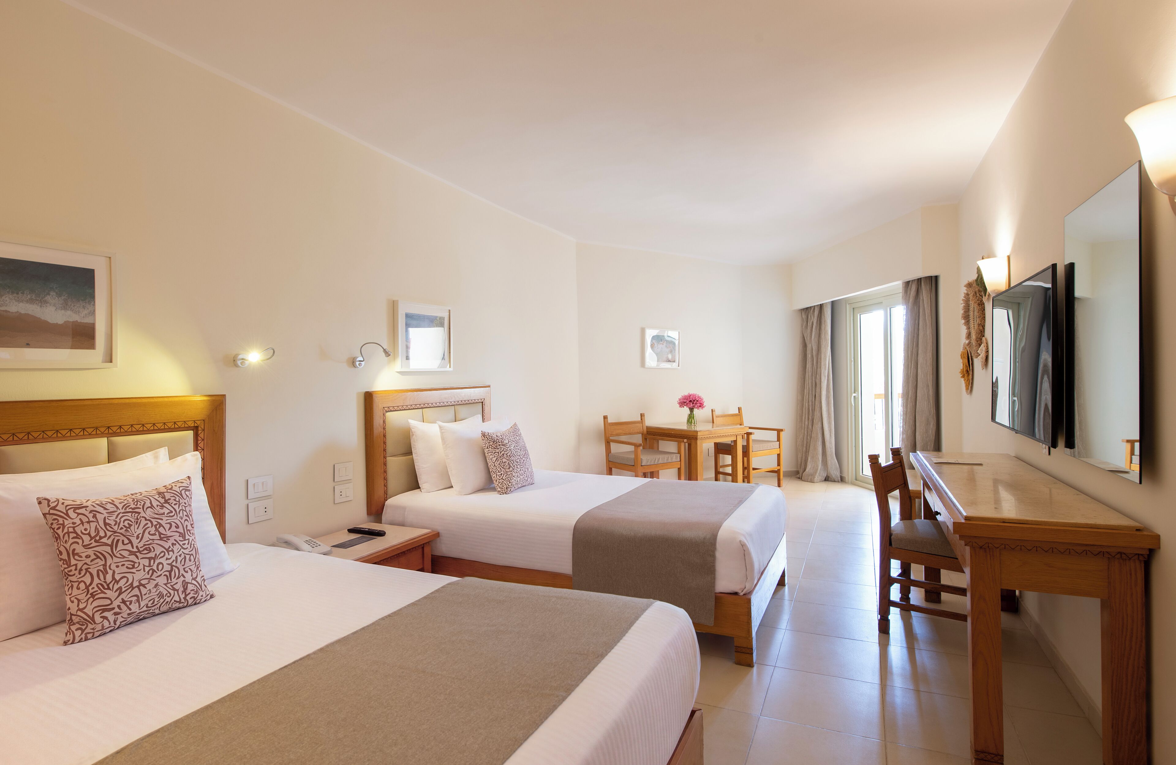 A hotel room with two beds, a desk, a chair, a TV, and a window with curtains.