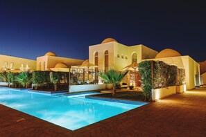A nighttime view of a hotel with a swimming pool, outdoor seating, and a desert landscape in the background. - Fort Arabesque Resort, Spa & Villas (Makadi Bay)