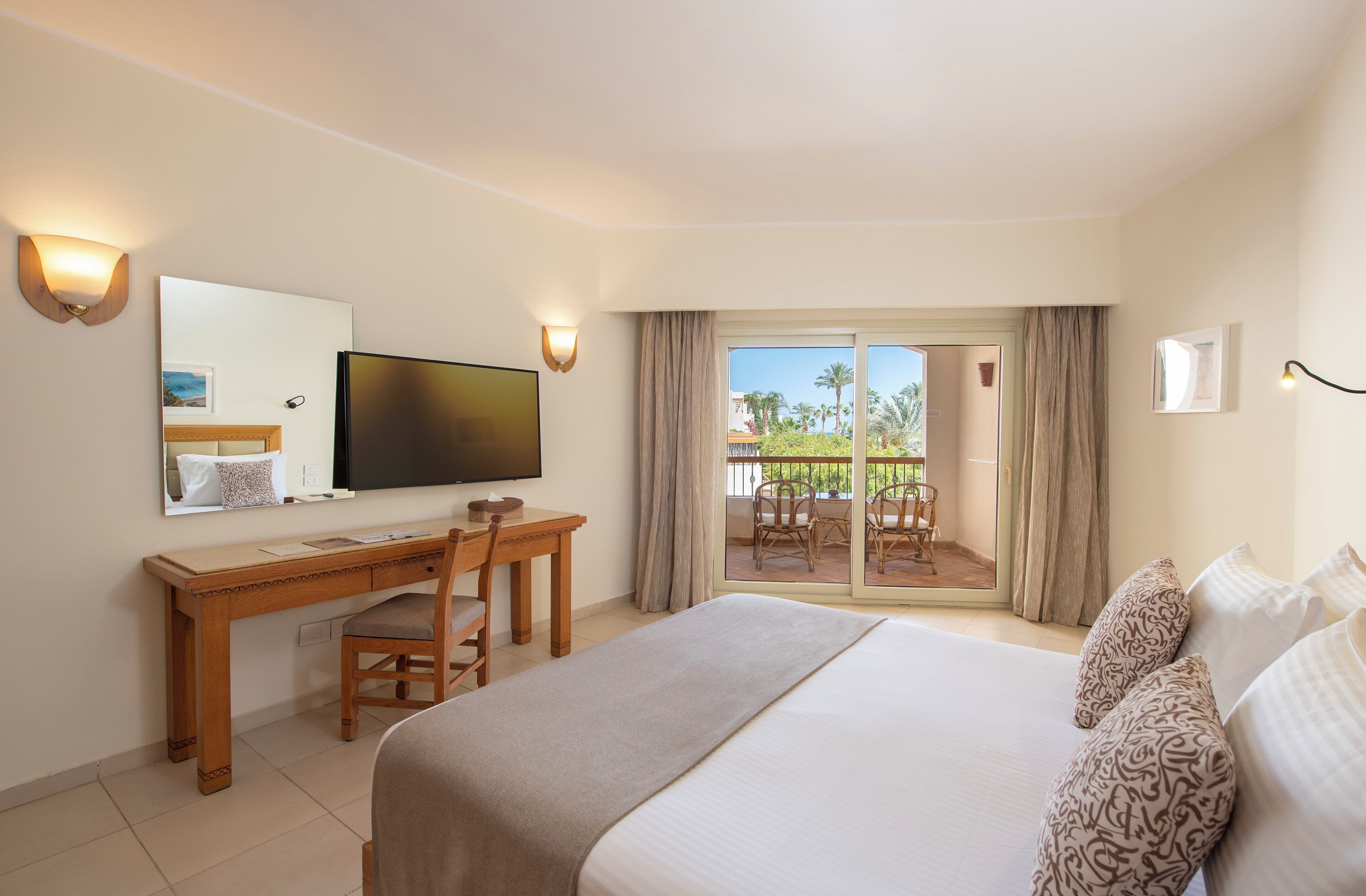 A hotel room with a bed, a desk, a television, and a balcony with a view.