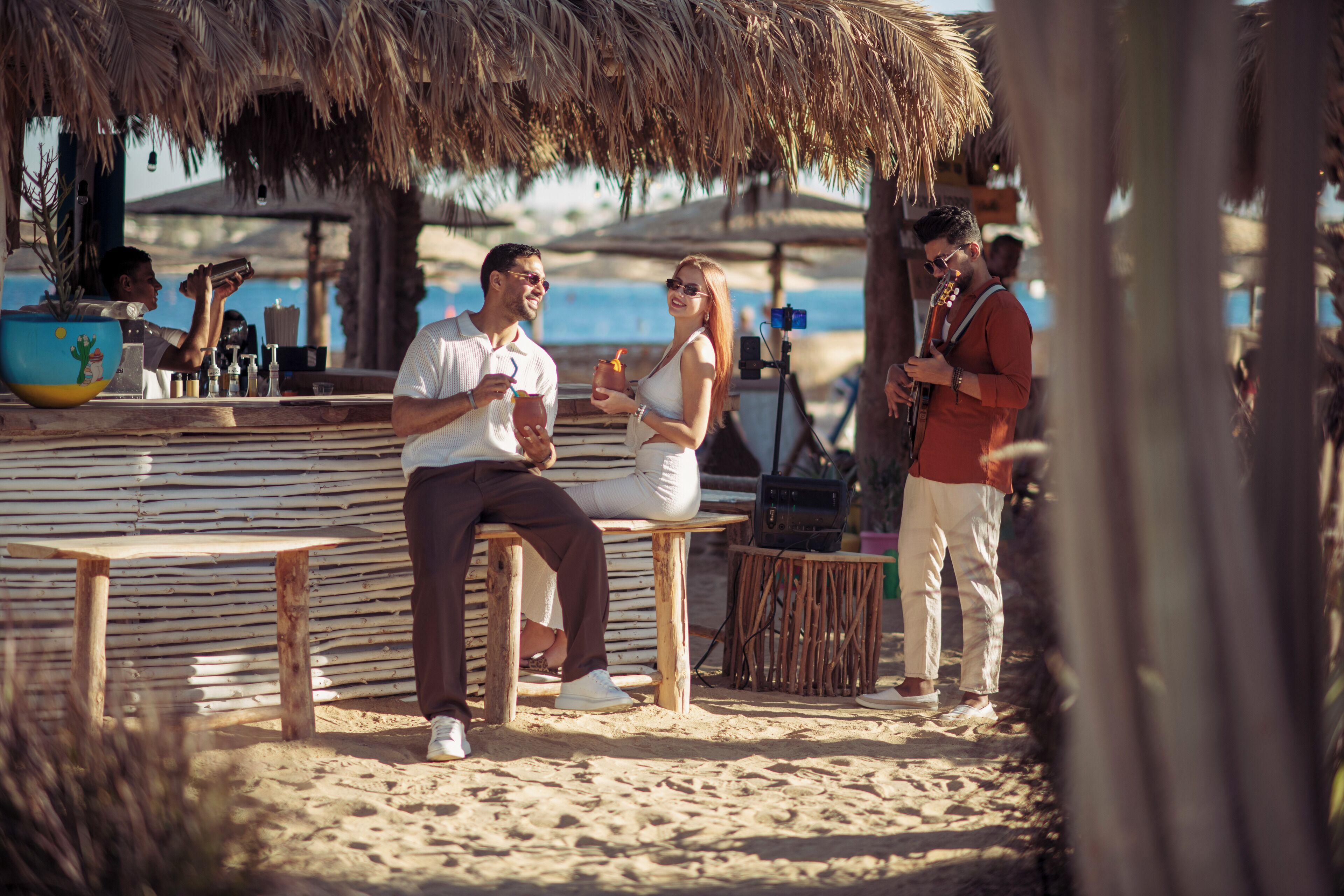 Un bar en la playa con bancos de madera y techo de paja.