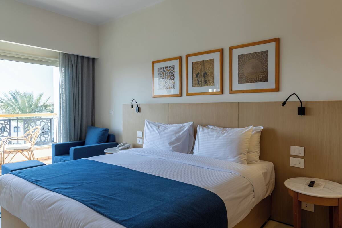 Ett hotellrum med en stor säng, en sittgrupp med en fåtölj, ett litet bord och två inramade tavlor på väggen.