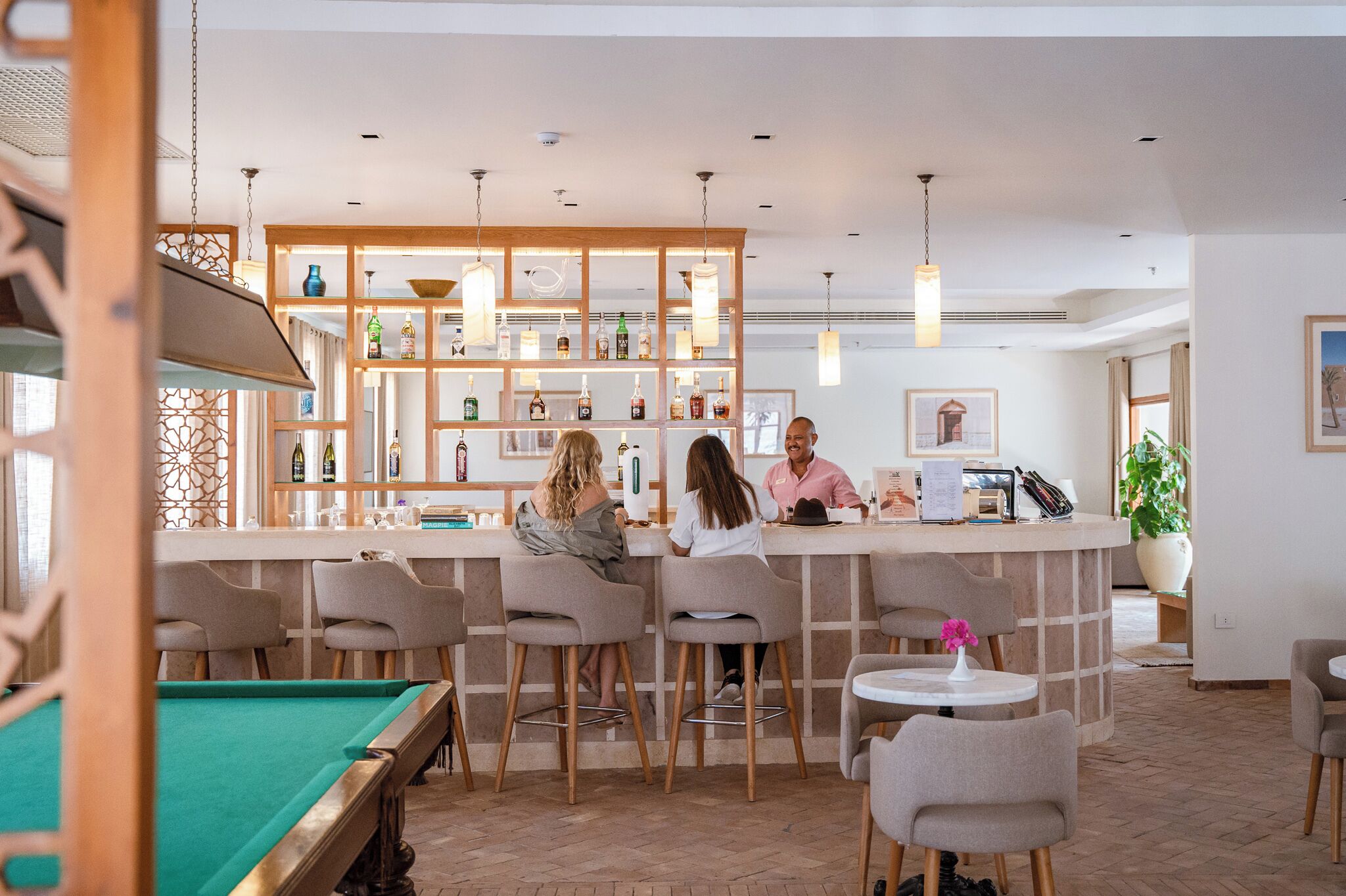 A bar area with a pool table, bar stools, and a bartender.