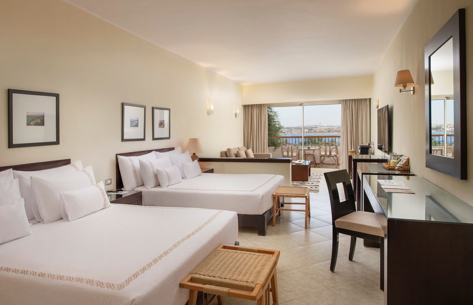 Habitación de hotel con dos camas, un escritorio, una silla, una mesita y vista al mar.
