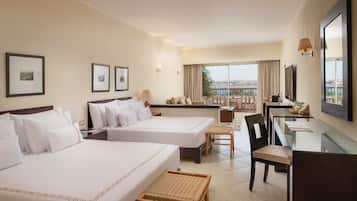 Habitación de hotel con dos camas, un escritorio, una silla, una mesita y vista al mar.