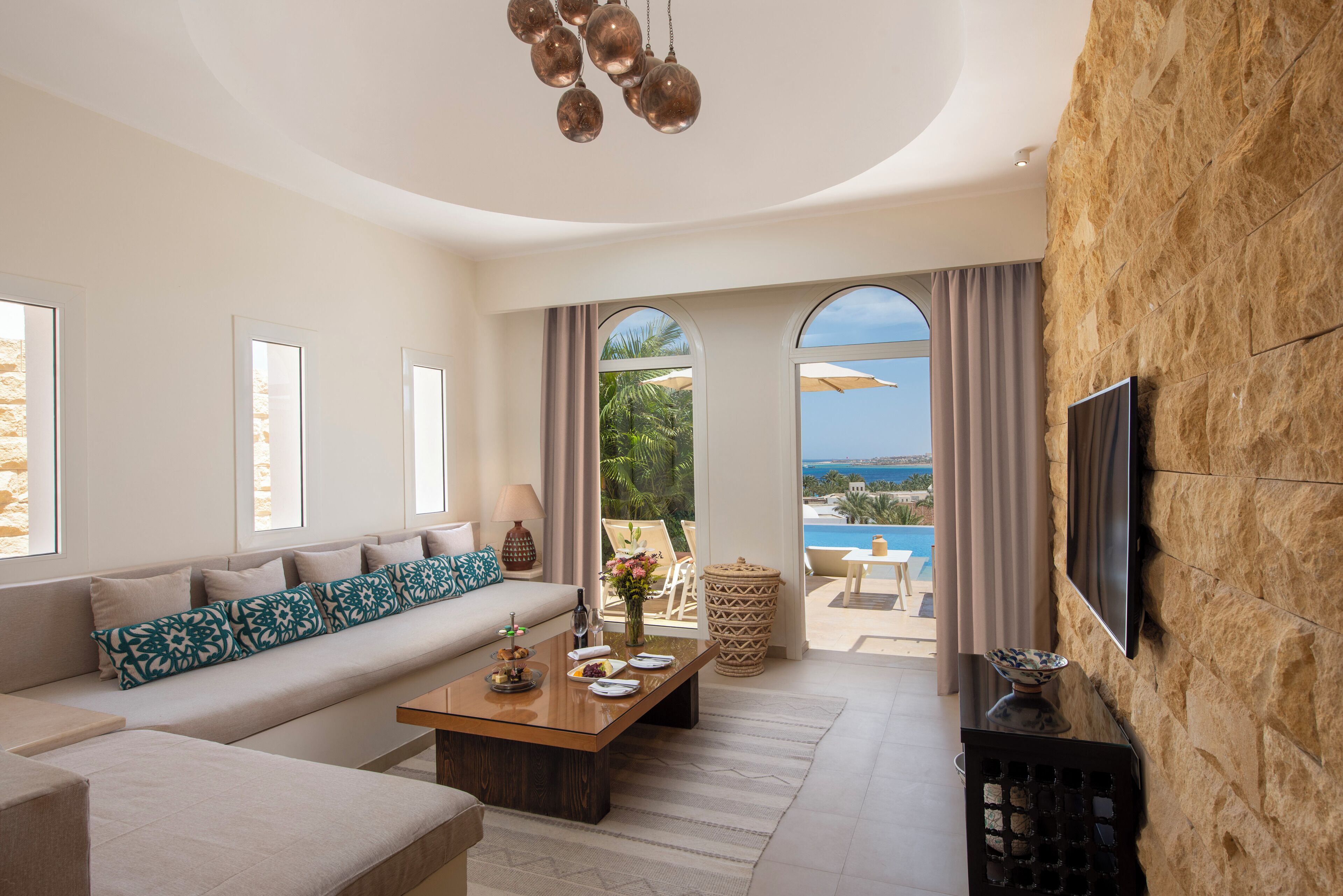 A modern living room with a sofa, coffee table, and a TV mounted on a stone wall.
