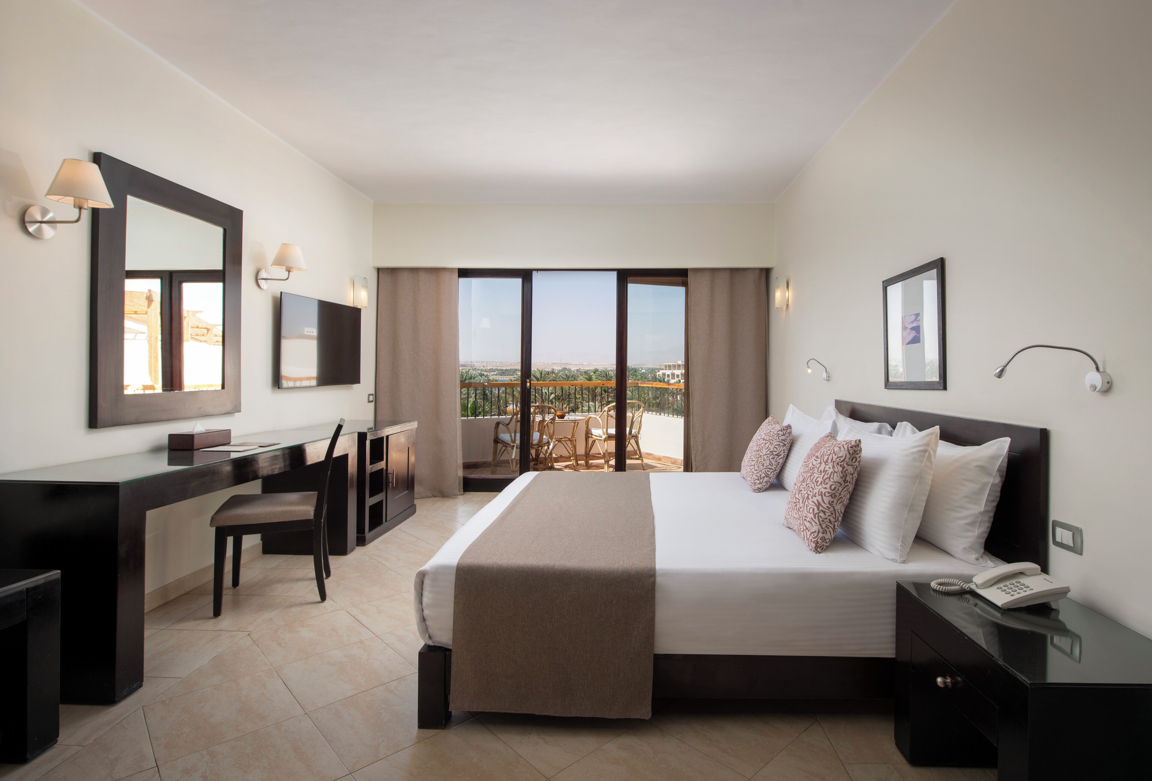 A hotel room with a bed, desk, chair, and a balcony with a view.