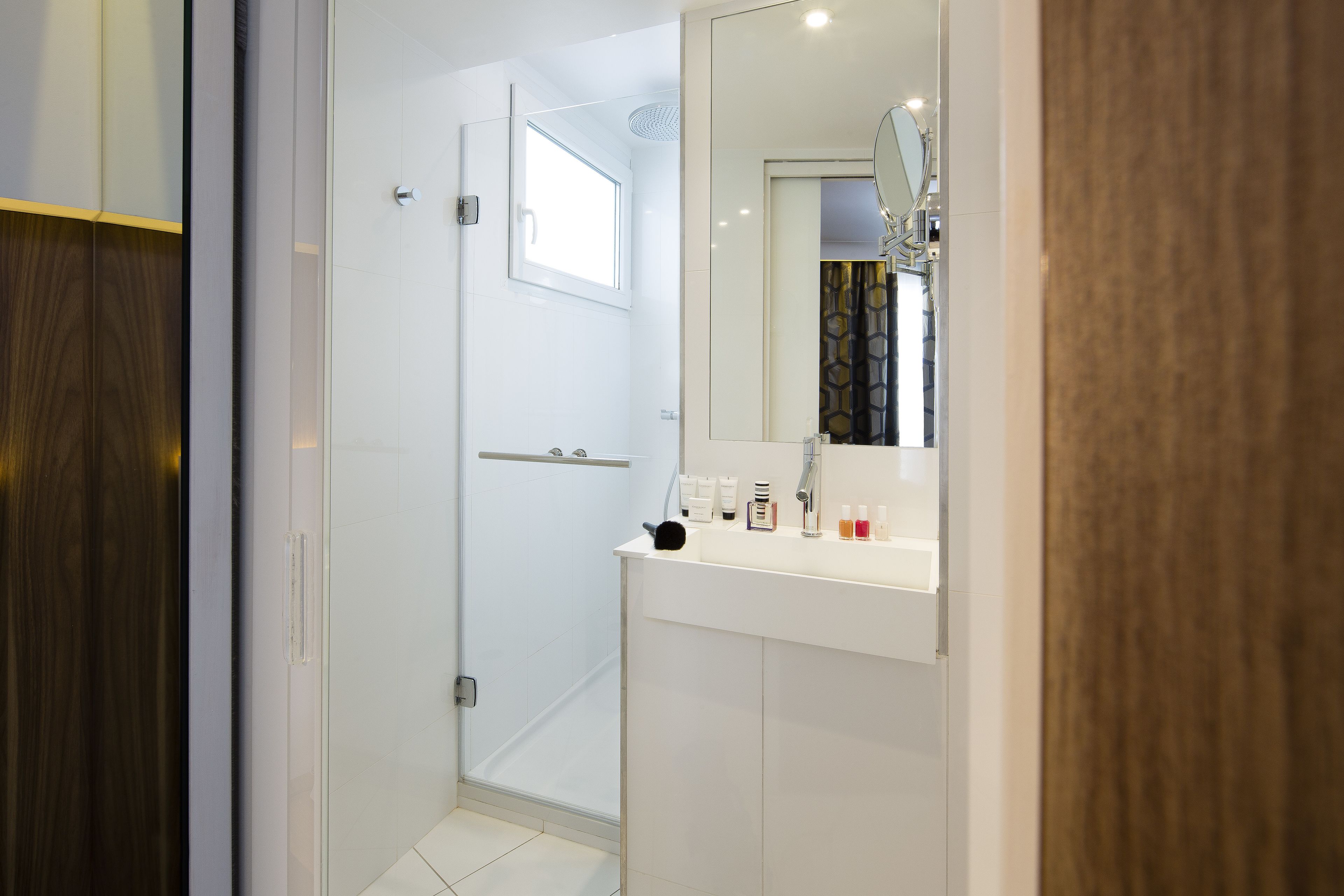 Un baño moderno con cabina de ducha de vidrio, tocador blanco con espejo y puerta de madera.