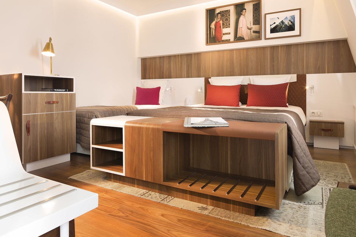 A modern bedroom with a wooden headboard, a bedside table, a lamp, and a bed with red pillows.