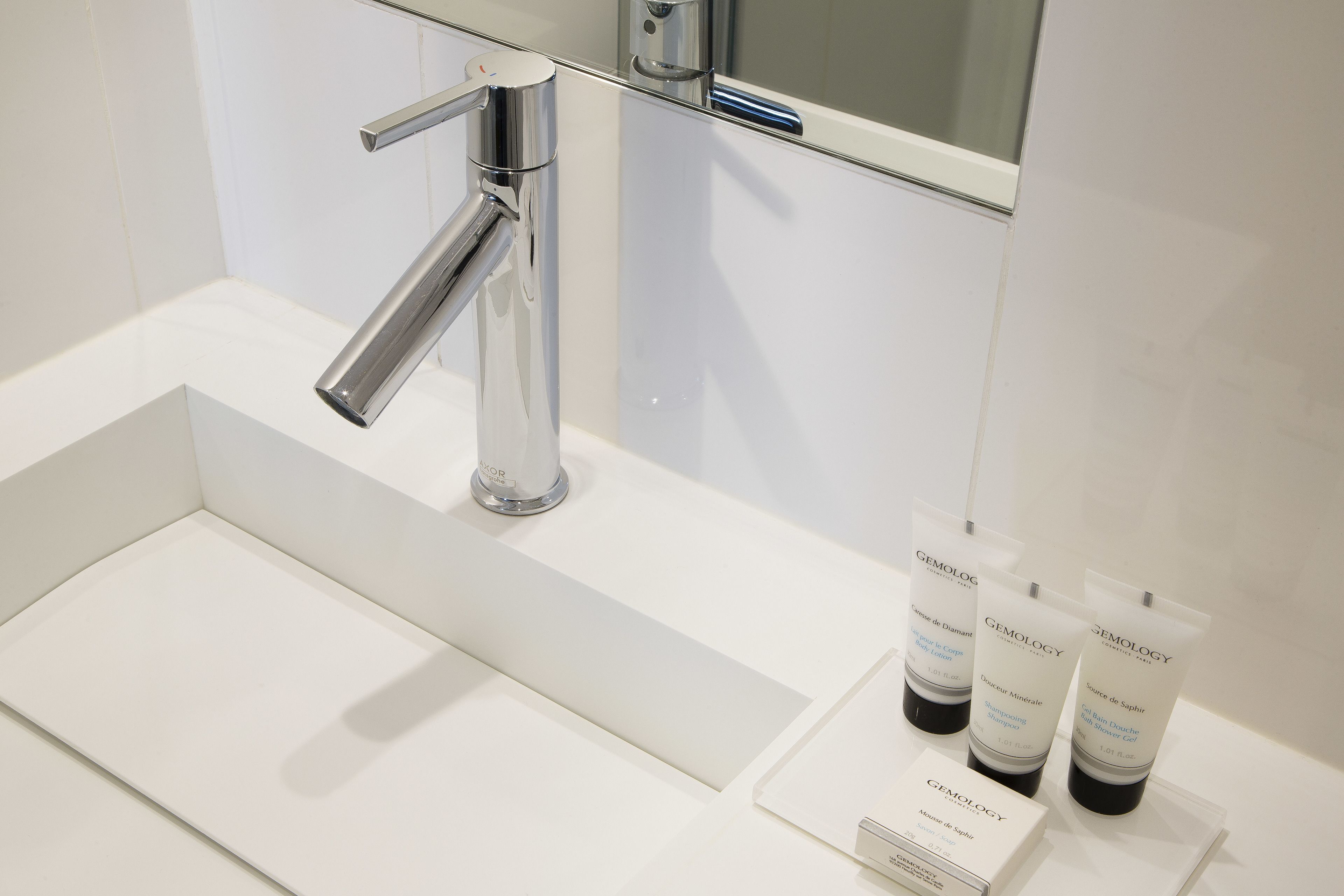 Un baño moderno con grifo cromado, lavamanos blanco y tres productos de cuidado de la piel Gemology sobre el mostrador.