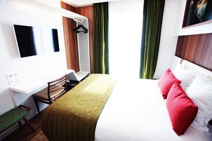 Habitación de hotel con cama, escritorio, laptop, silla y televisor montado en la pared.