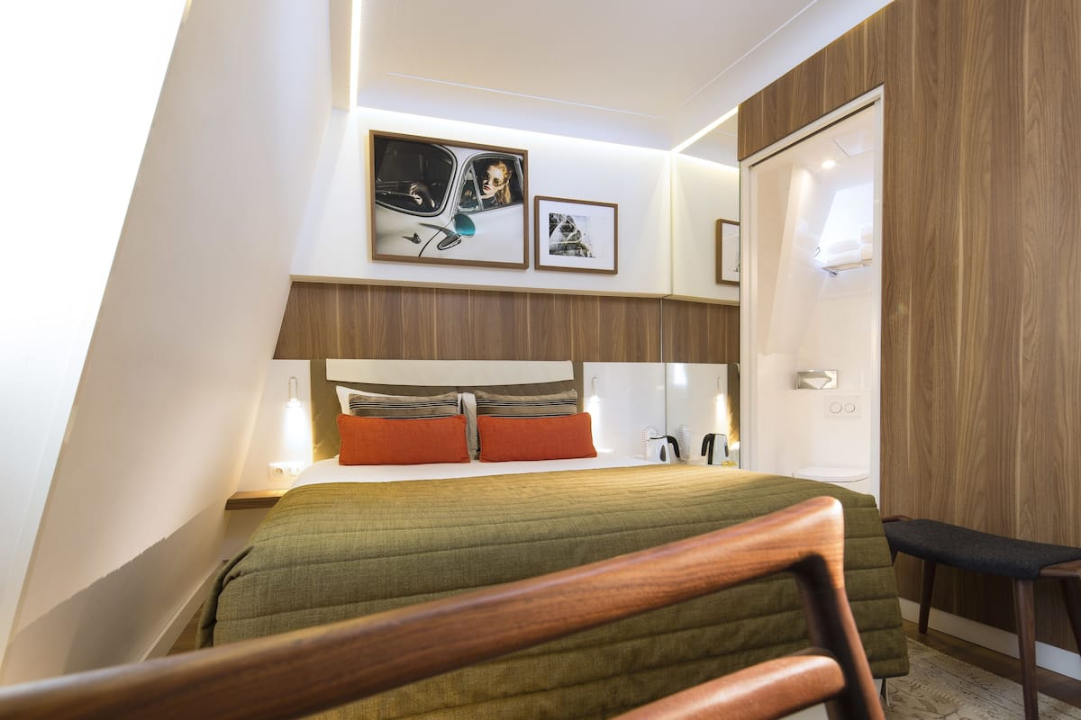 A modern hotel room with a bed, bedside table, and a wooden headboard.