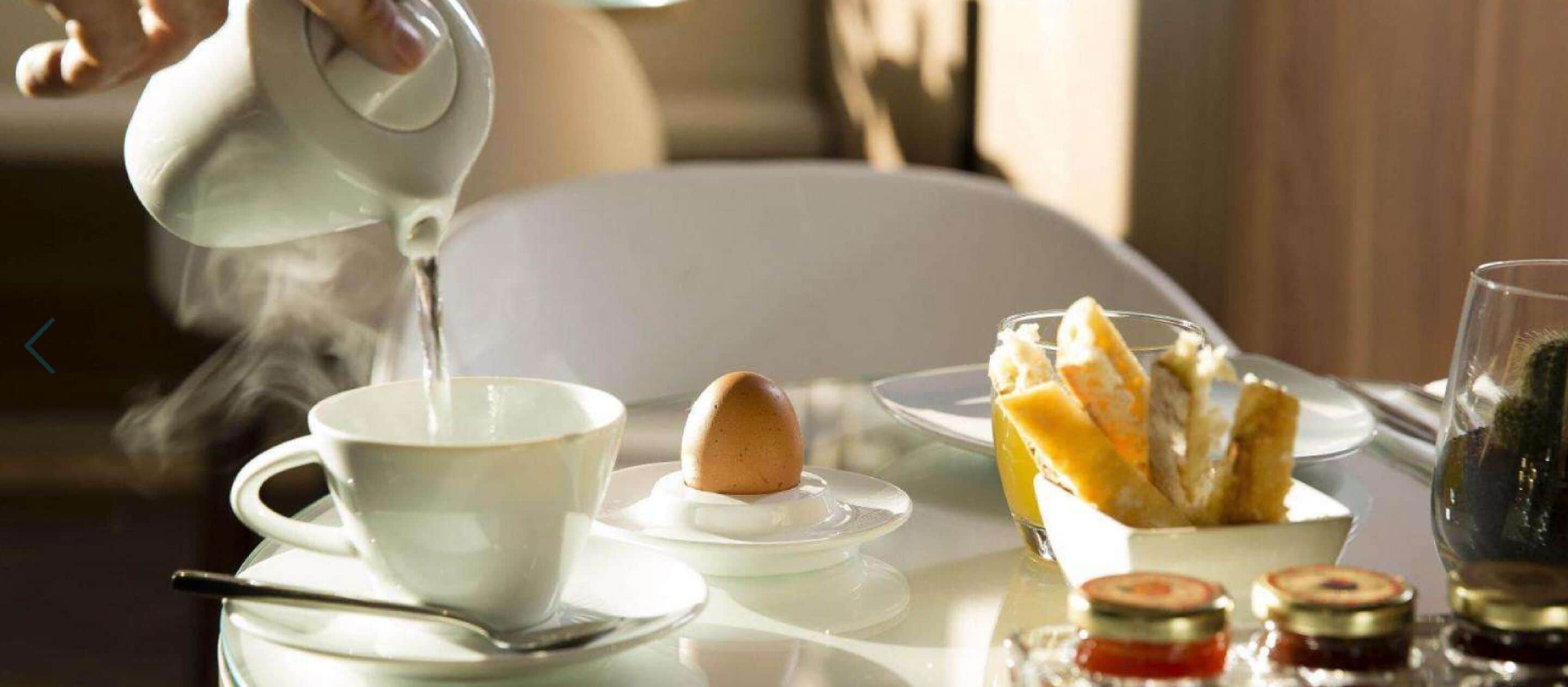 A breakfast setting with a cup of hot beverage, a plate with a croissant, and a bowl of fruit.