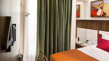 Hotellihuone, jossa on sänky, työpöytä, tuoli, ikkuna verhoilla ja taulu seinällä.