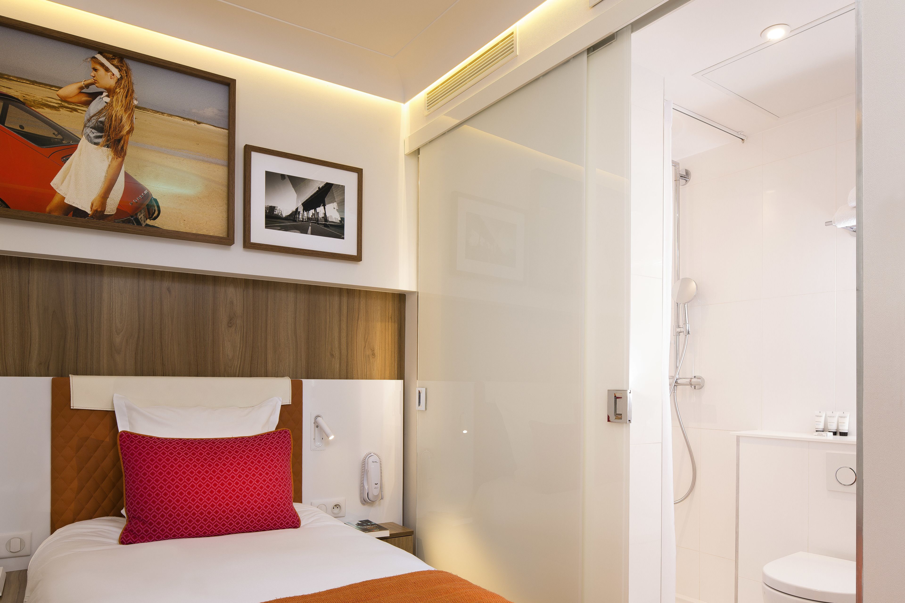 Une chambre d’hôtel comprenant un lit, une table de chevet, un téléphone, un tableau encadré et un espace douche.