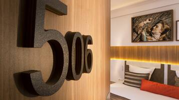 Une chambre d’hôtel avec un grand panneau en bois indiquant le numéro de la chambre, un lit avec des oreillers à rayures et un tableau accroché au mur.
