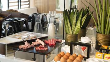 A breakfast buffet with various food items, coffee machines, and decorative plants.