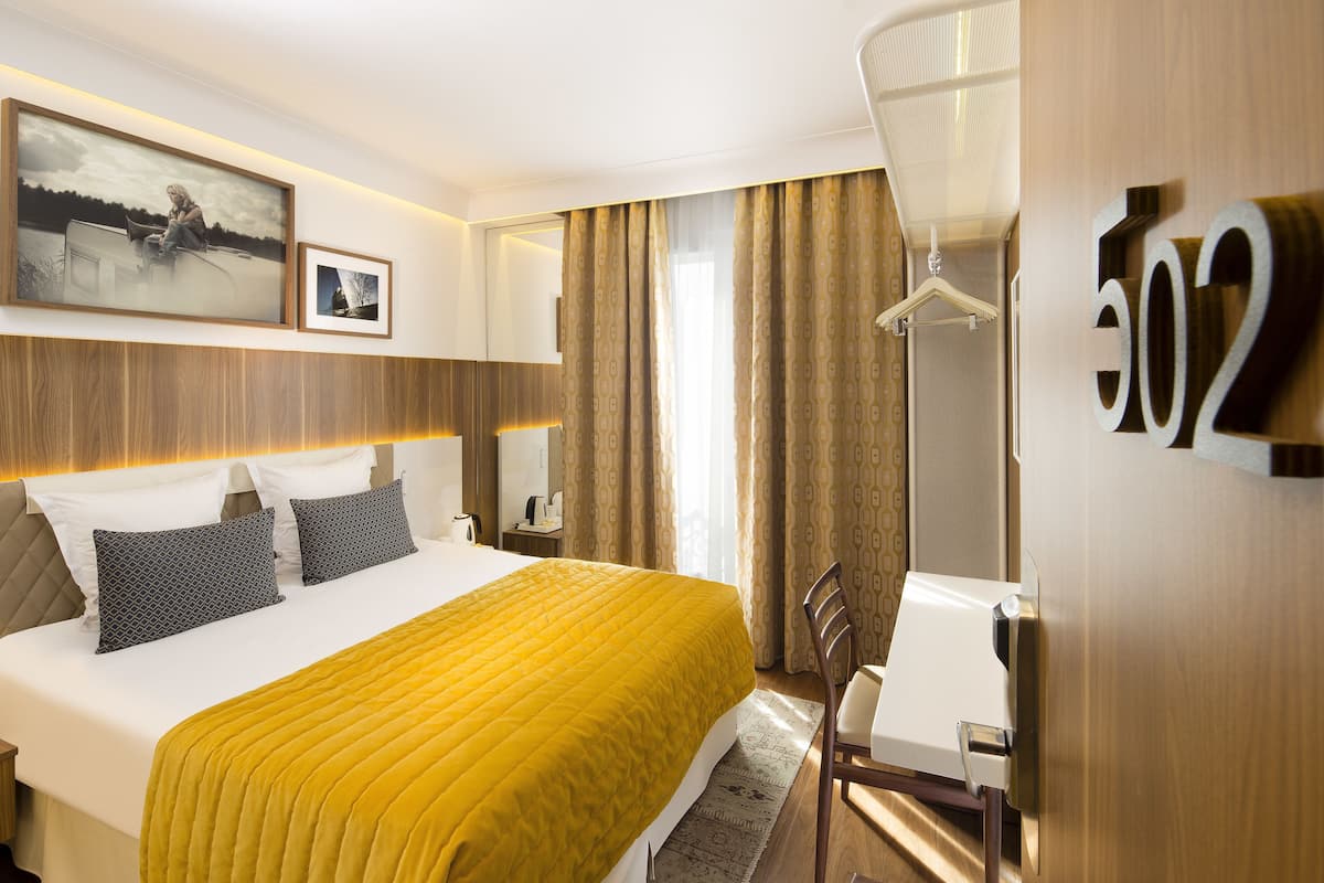 A hotel room with a large bed, a desk, and a chair. There is a number sign on the wall and a picture on the wall.