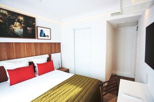 A hotel room with a bed, a desk, a chair, a TV, and a door.