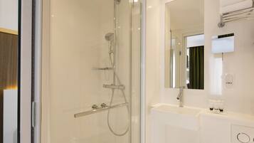 Une salle de bain moderne avec une douche à parois de verre, un lavabo blanc et un grand miroir.