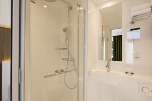 Un baño moderno con ducha de vidrio, lavamanos blanco y espejo grande.