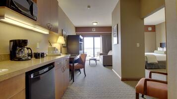 A hotel room with a kitchenette, a dining area, a living room with a sofa, and a separate bedroom.