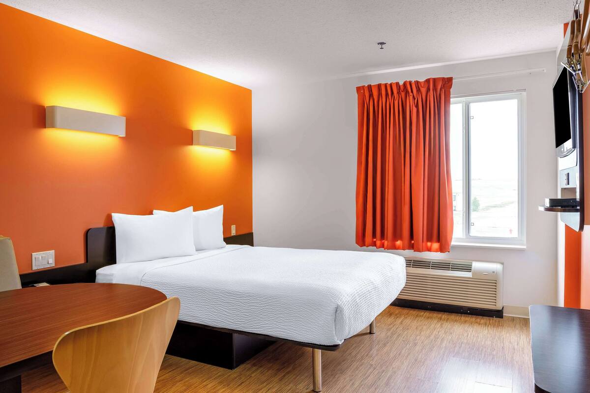 Une chambre d’hôtel équipée d’un lit, d’un bureau, d’une chaise, d’un appareil de climatisation et d’une fenêtre avec des rideaux.
