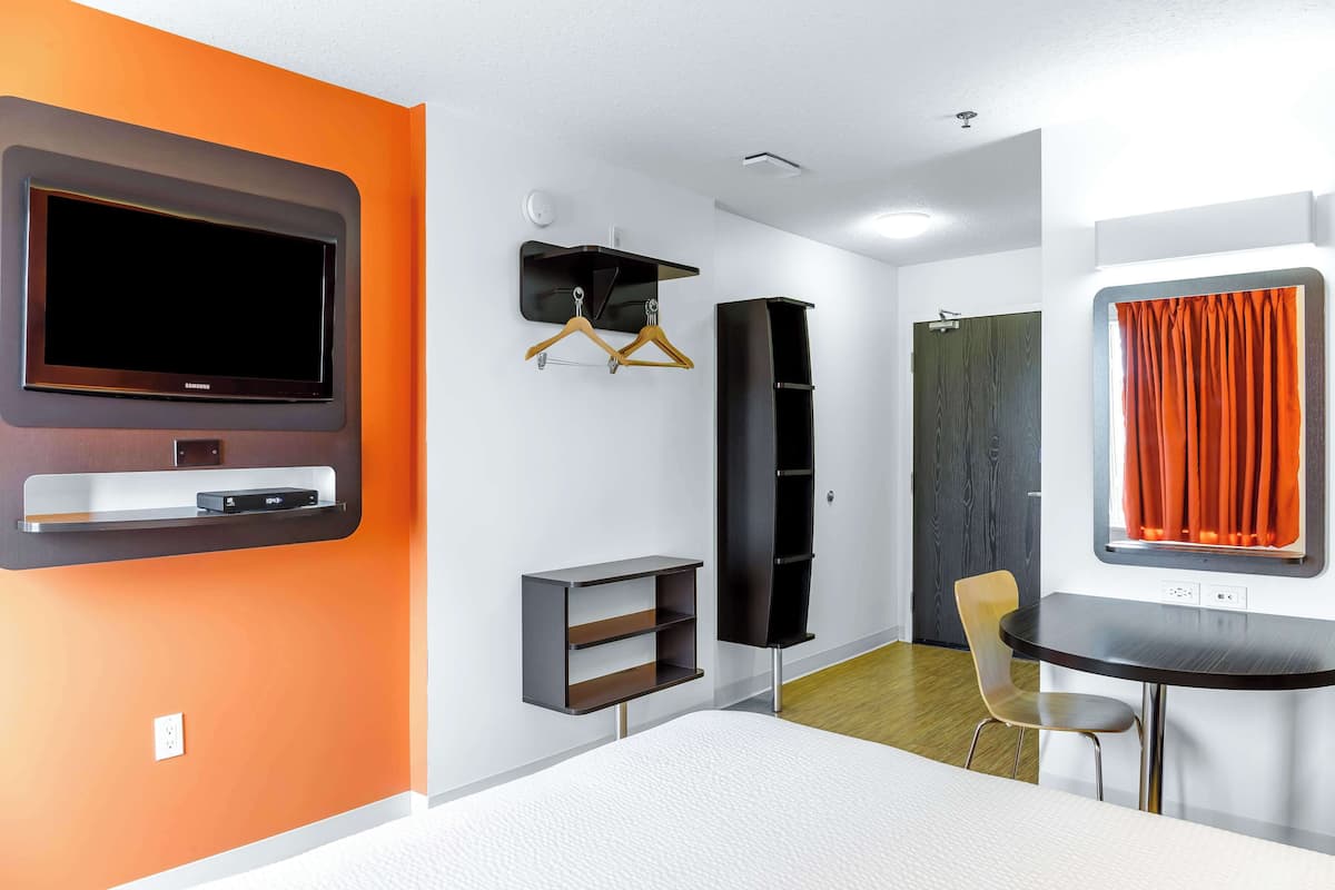 Une chambre moderne équipée d’un téléviseur à écran plat, d’une petite table, d’une chaise, d’une armoire et d’une fenêtre avec des rideaux.