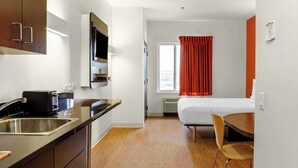 A compact hotel room with a kitchenette, a bed, a window with red curtains, and a small table with a chair. - Motel 6 Swift Current, SK (Swift Current)