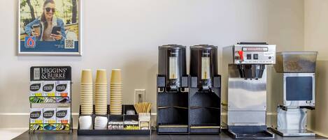 A coffee station with multiple coffee machines, disposable cups, and a display of coffee pods.