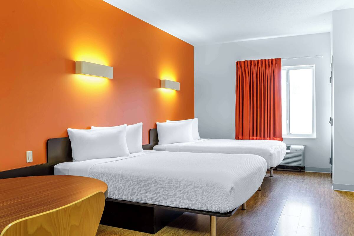 Une chambre d’hôtel avec deux lits, une table en bois et une fenêtre avec des rideaux orange.