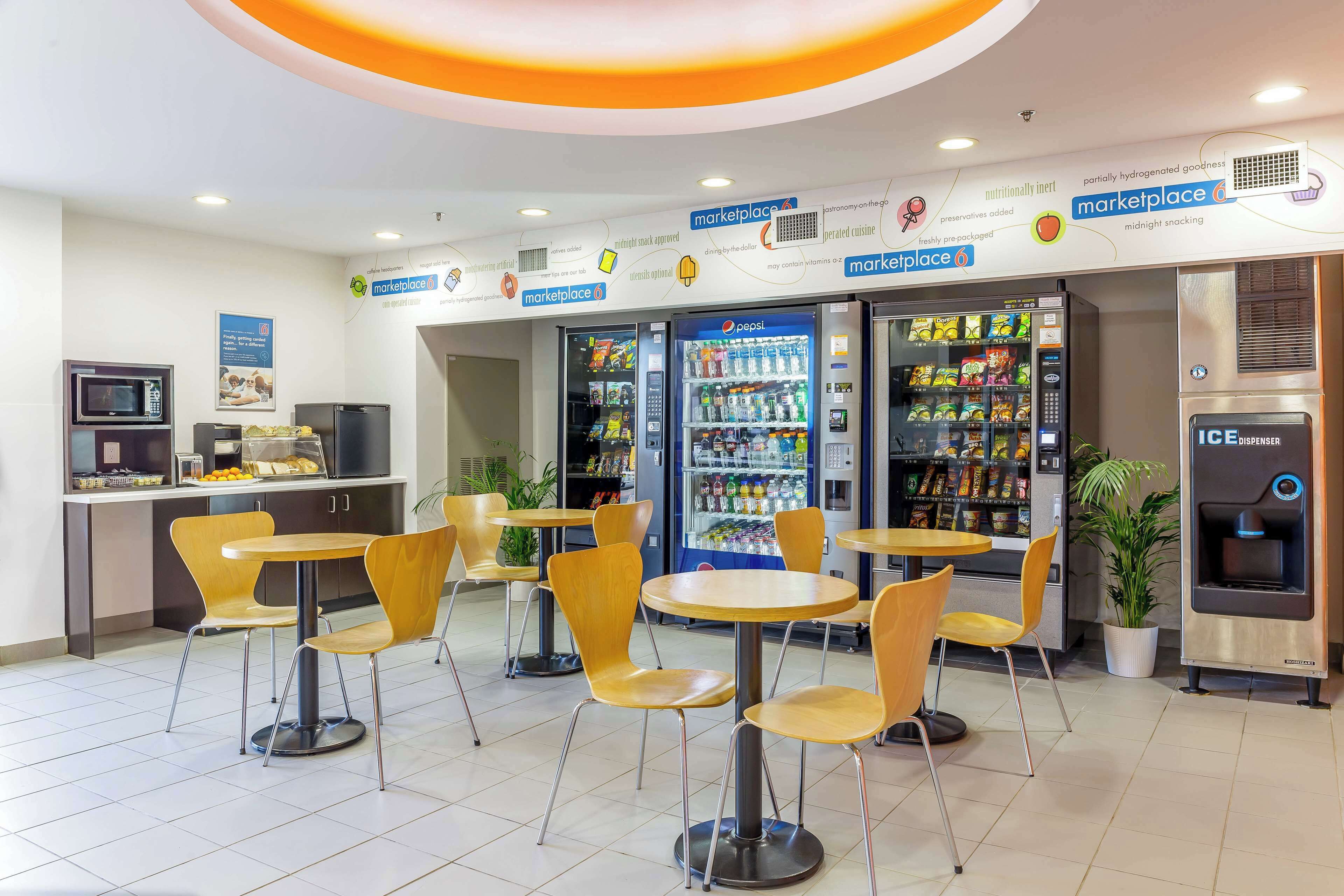 Un café moderne avec des tables rondes et des chaises jaunes, des distributeurs automatiques et un réfrigérateur rempli de produits Pepsi.