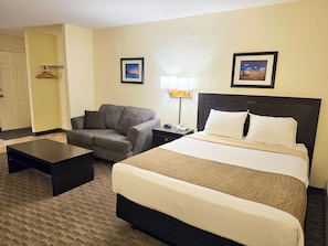 A hotel room with a bed, a chair, a nightstand, a lamp, and two framed pictures on the wall.