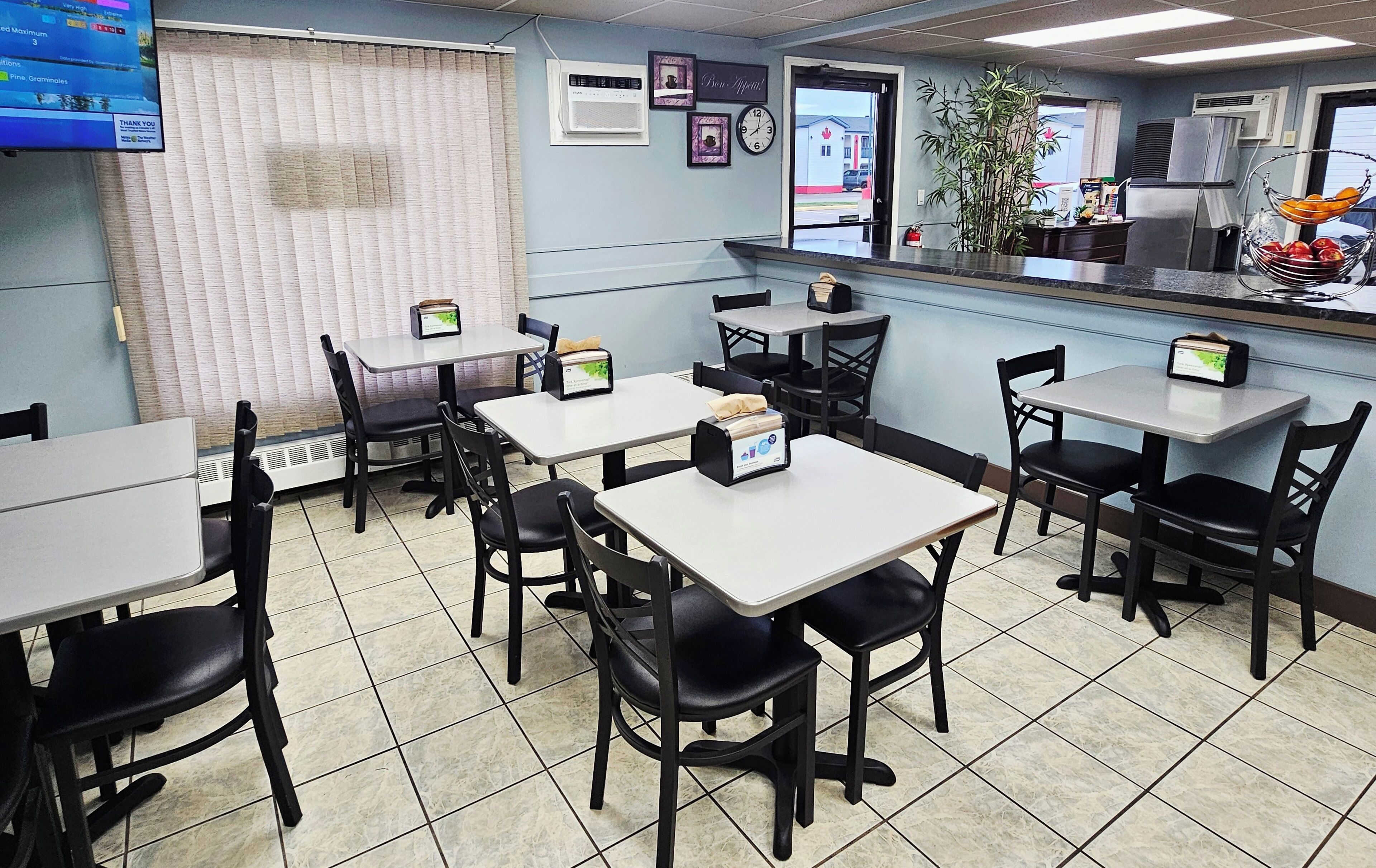A restaurant interior with multiple tables and chairs, a counter with a display, and a clock on the wall.