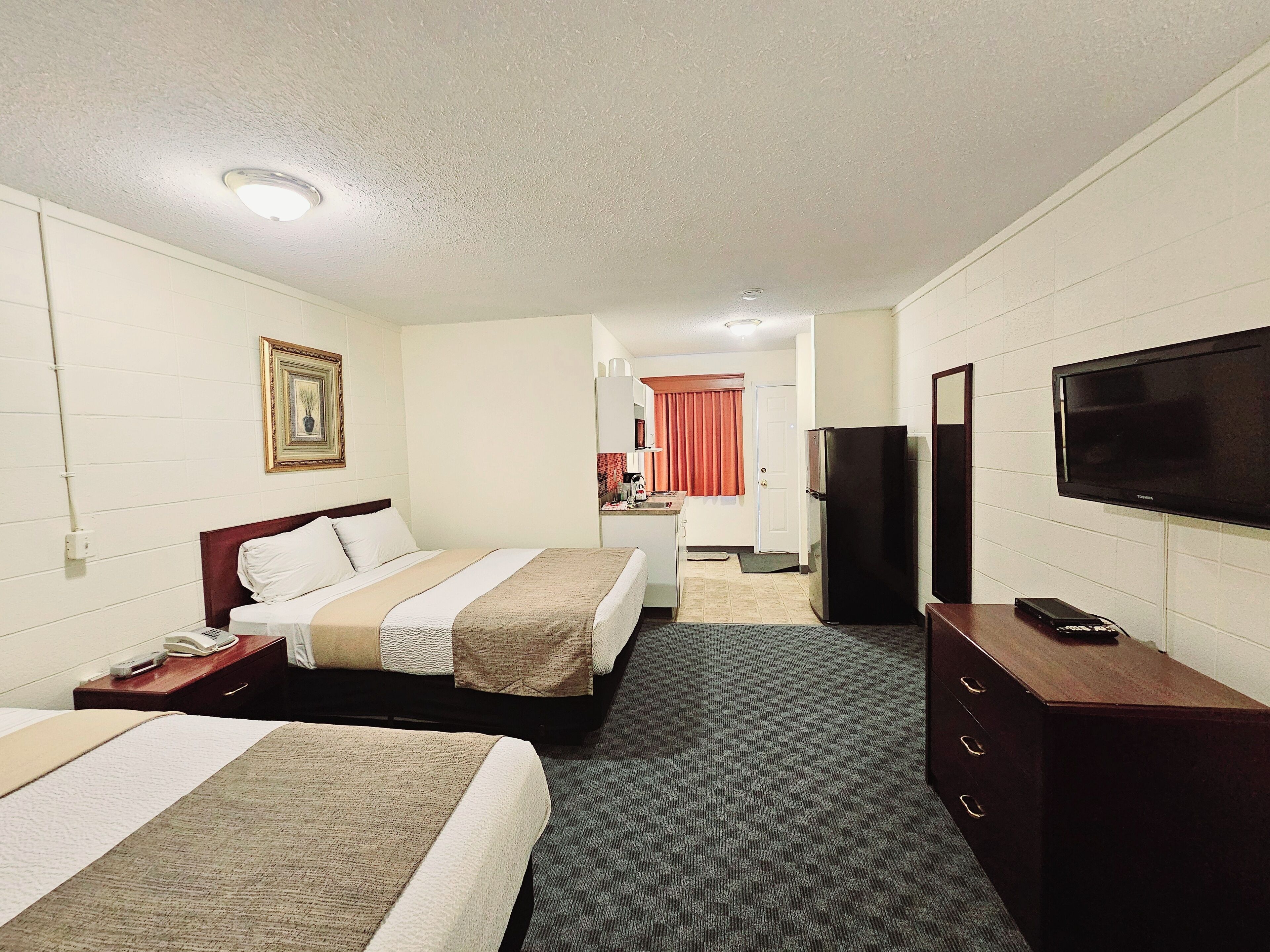 A hotel room with two beds, a television, a refrigerator, and a small kitchenette.