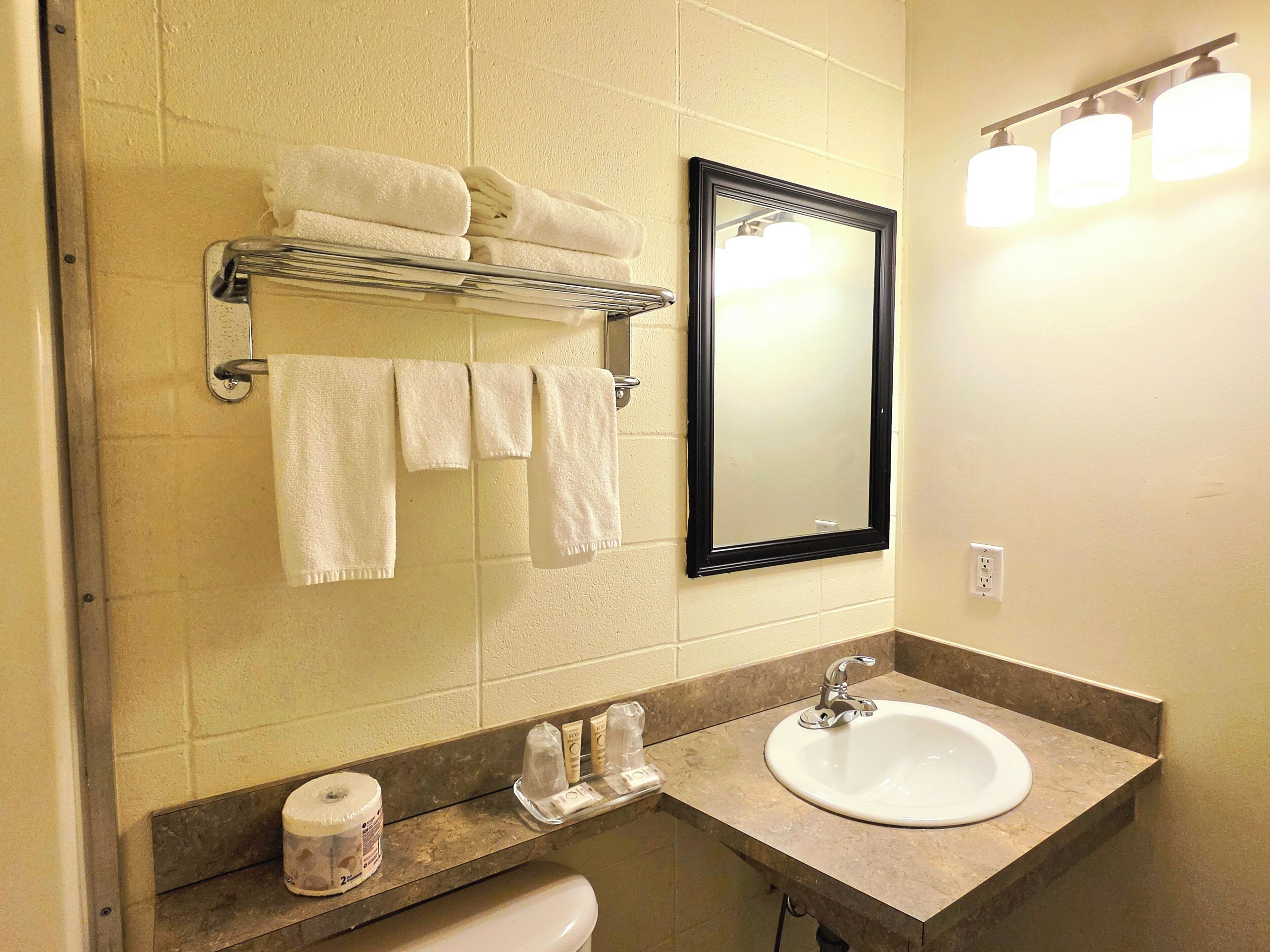 A bathroom with a sink, mirror, towel rack, and toiletries.