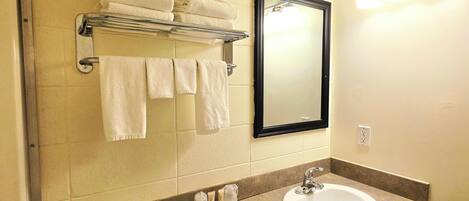 Un baño con lavamanos, espejo, toallero y artículos de aseo.
