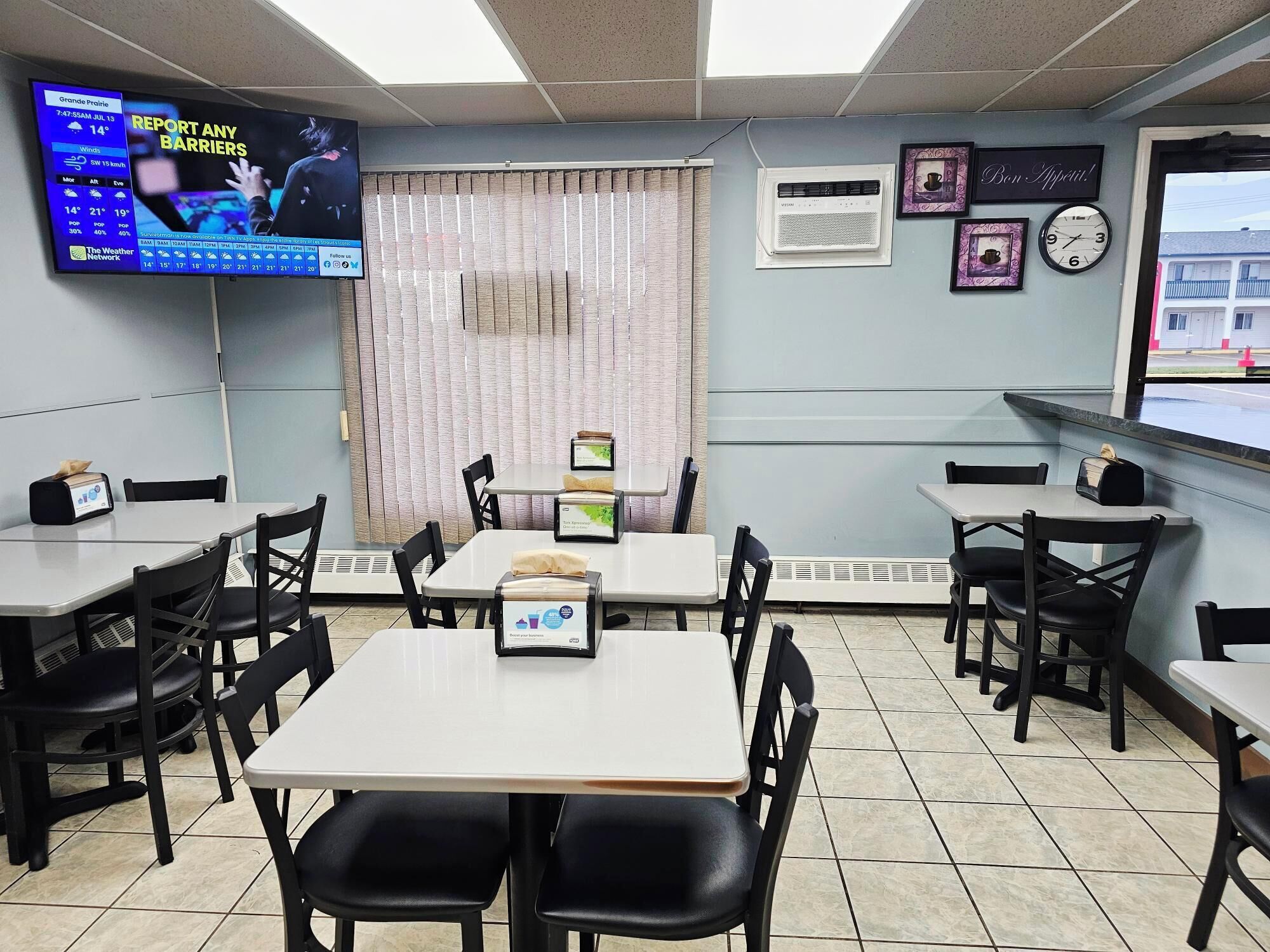 A restaurant interior with tables, chairs, a TV displaying weather, and a window with a view.